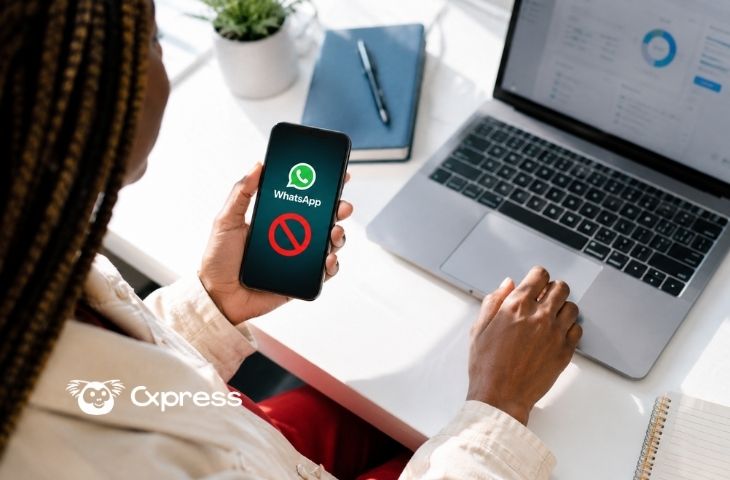 Mulher a segurar o telemóvel com o WhatsApp bloqueado no ecrã enquanto está a utilizar o portátil com um painel aberto