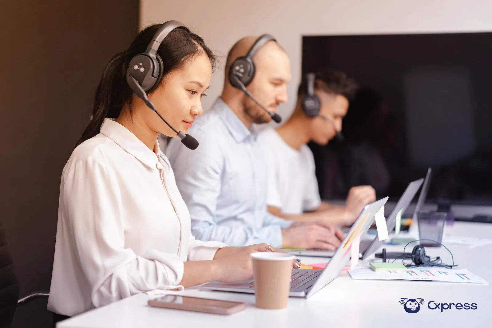 Agentes de apoio ao cliente a trabalhar com computadores e painel de atendimento